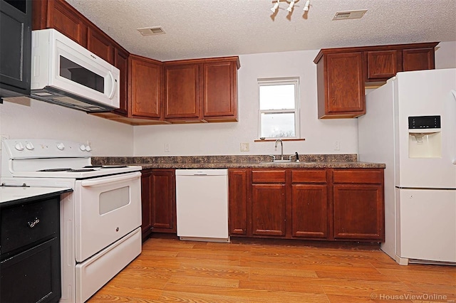 kitchen featuring visible vents, light wood-style flooring, white appliances, and a sink