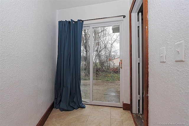 doorway to outside featuring light tile patterned floors, a textured wall, and baseboards