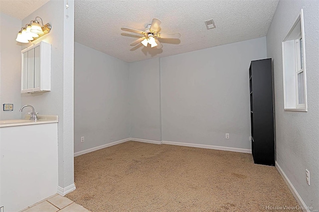 spare room with light carpet, a ceiling fan, visible vents, and a textured ceiling