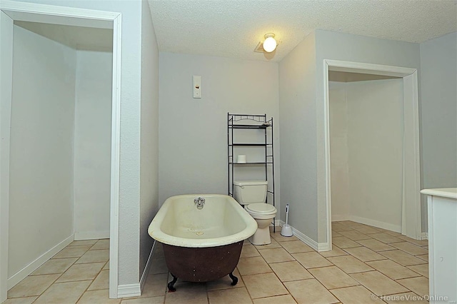 bathroom with baseboards, toilet, a freestanding tub, tile patterned floors, and a textured ceiling