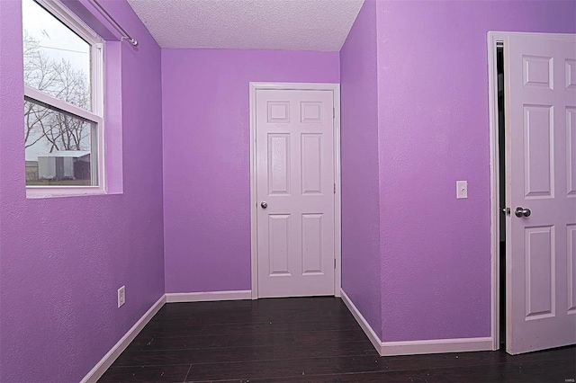 hall with dark wood-type flooring, a textured wall, baseboards, and a textured ceiling