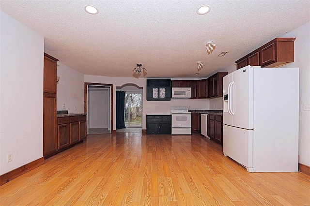 kitchen featuring white appliances, dark countertops, light wood-style floors, and arched walkways