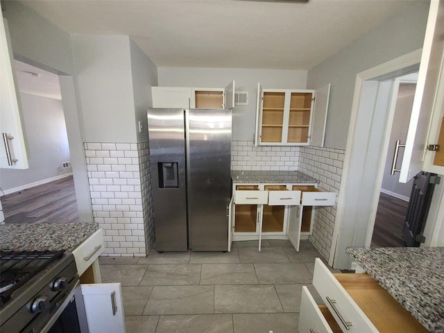 kitchen featuring visible vents, backsplash, stainless steel fridge, white cabinets, and light stone countertops