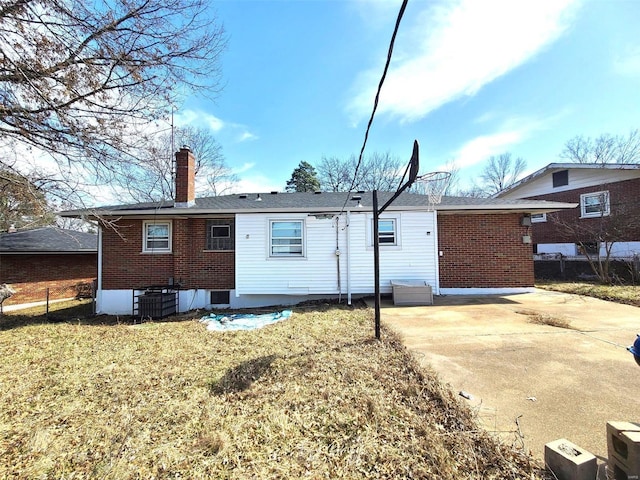 rear view of house featuring cooling unit, brick siding, a yard, and a chimney