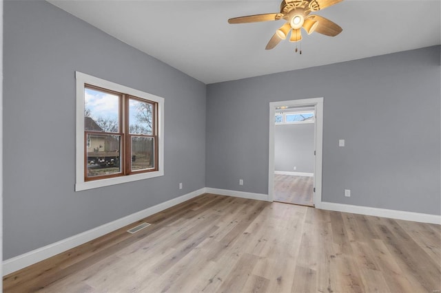 empty room featuring a ceiling fan, visible vents, light wood-style floors, and baseboards