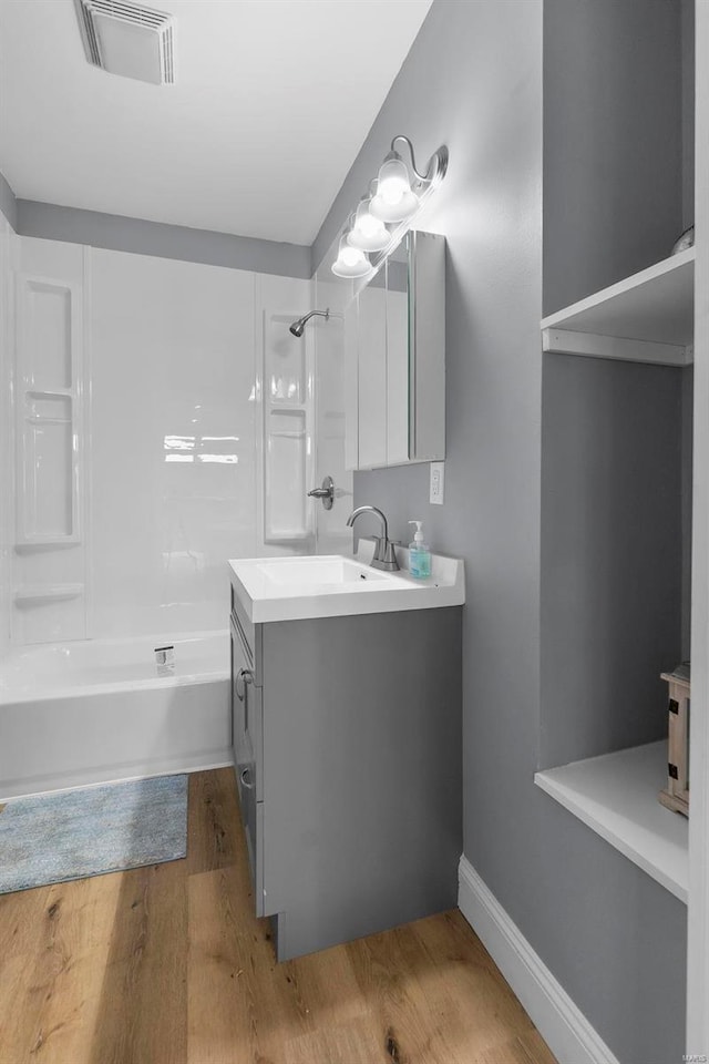 bathroom featuring visible vents, baseboards, bathtub / shower combination, wood finished floors, and vanity