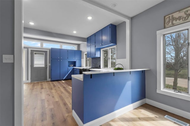 kitchen featuring light wood finished floors, blue cabinets, visible vents, and backsplash