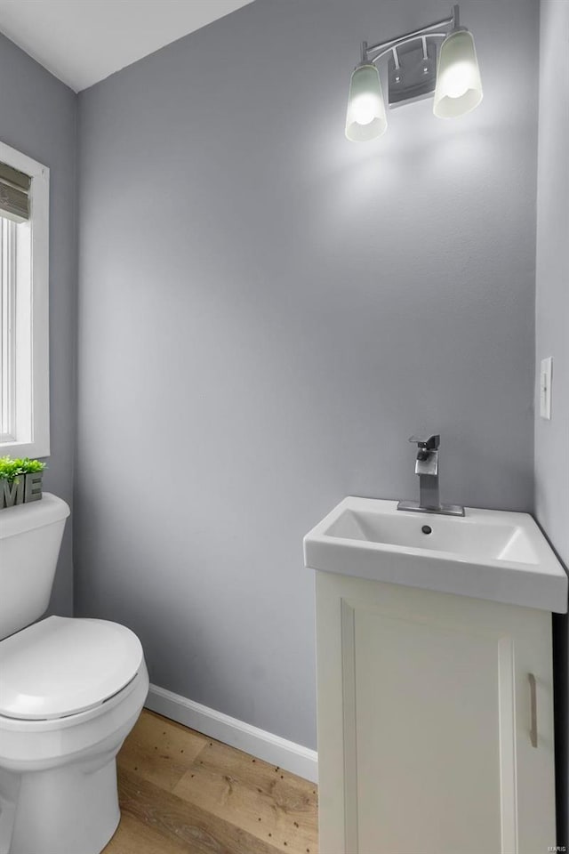 half bath with toilet, vanity, baseboards, and wood finished floors