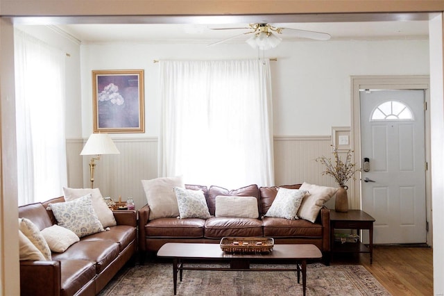 living area with wainscoting, crown molding, ceiling fan, and wood finished floors