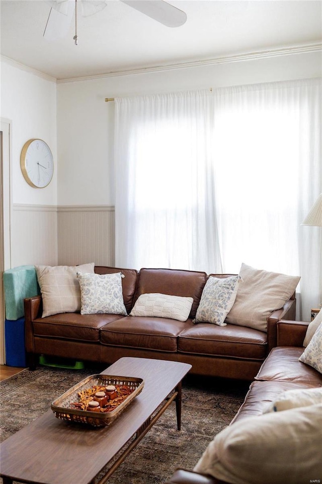 living area featuring crown molding, a ceiling fan, and a wainscoted wall