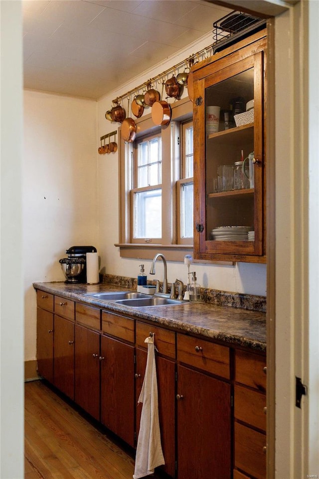 kitchen with a sink, light wood-type flooring, brown cabinets, and dark countertops