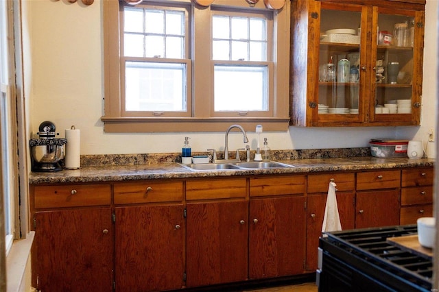 kitchen featuring brown cabinets, a sink, black gas range, dark countertops, and glass insert cabinets