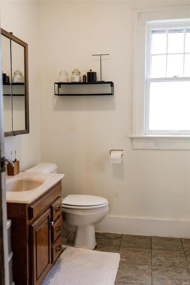 half bathroom with baseboards, toilet, a healthy amount of sunlight, and vanity