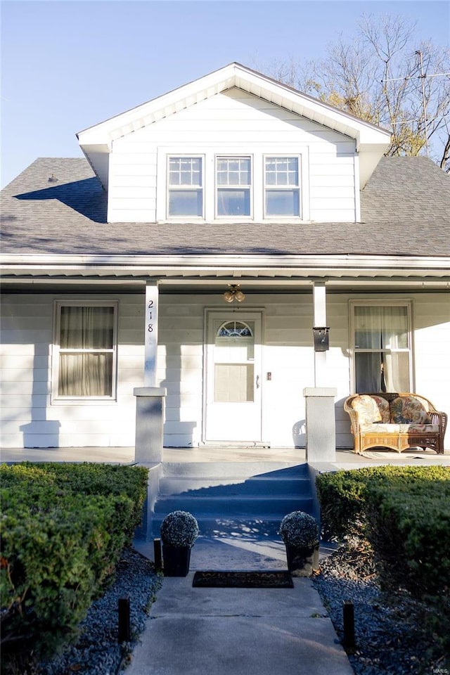 entrance to property featuring covered porch and a shingled roof