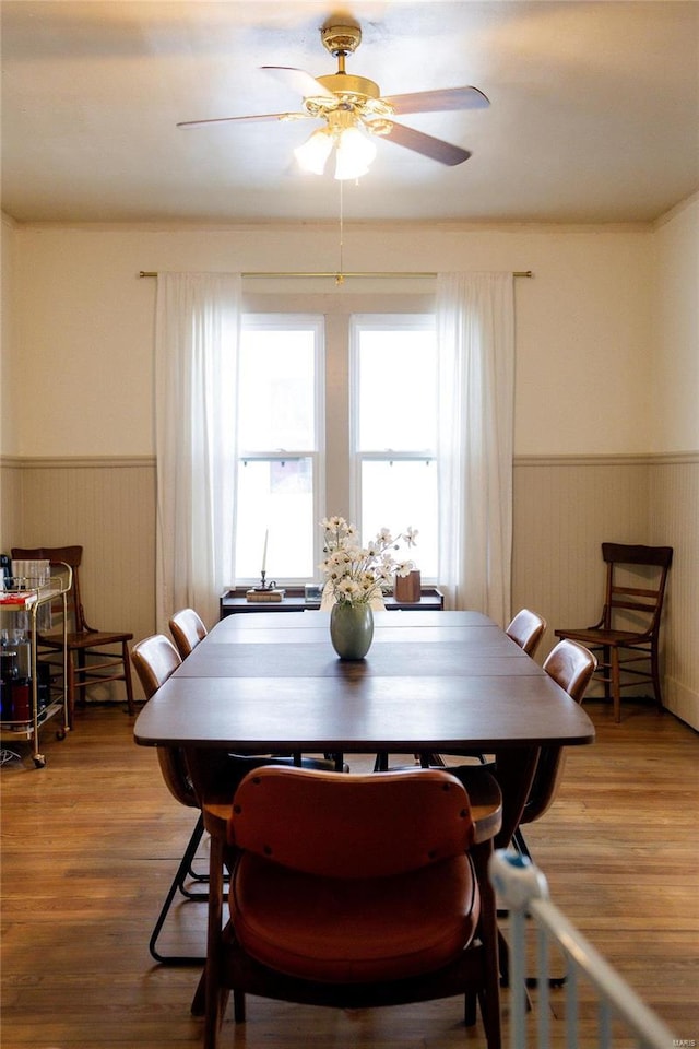 dining space with a wainscoted wall, wood finished floors, and a ceiling fan