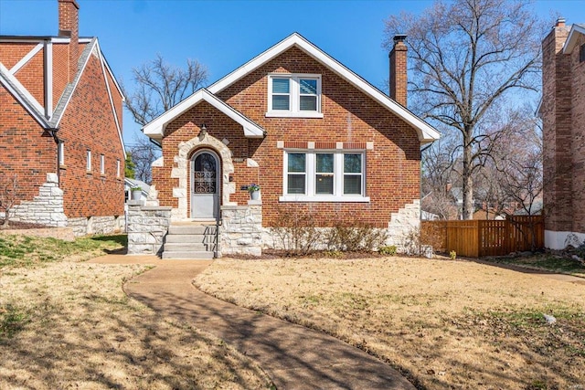 english style home with a front lawn, brick siding, a chimney, and fence