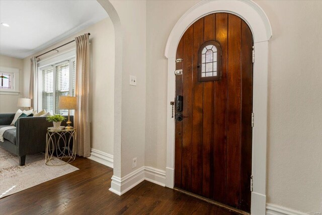 entryway with arched walkways, dark wood-type flooring, and baseboards