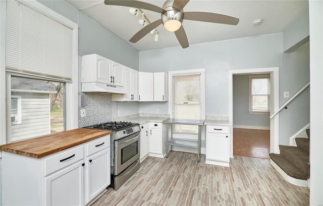 kitchen with a ceiling fan, butcher block counters, stainless steel gas range oven, under cabinet range hood, and white cabinets