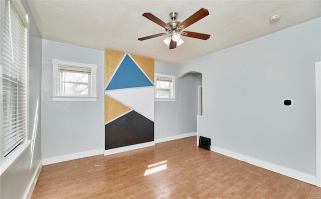 spare room featuring baseboards, wood finished floors, arched walkways, and a ceiling fan