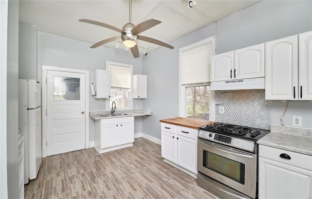 kitchen with stainless steel range with gas stovetop, under cabinet range hood, decorative backsplash, a sink, and freestanding refrigerator