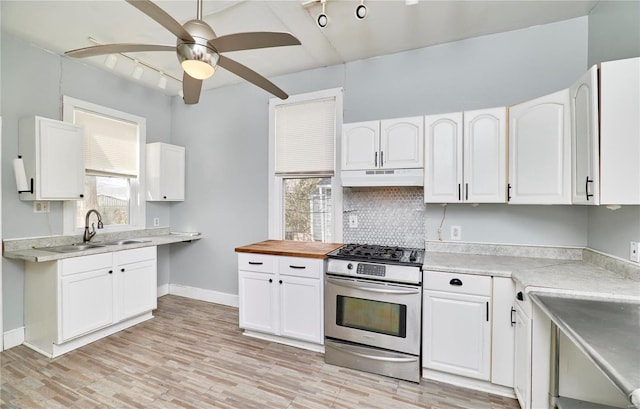 kitchen with a sink, stainless steel gas range, white cabinetry, under cabinet range hood, and ceiling fan