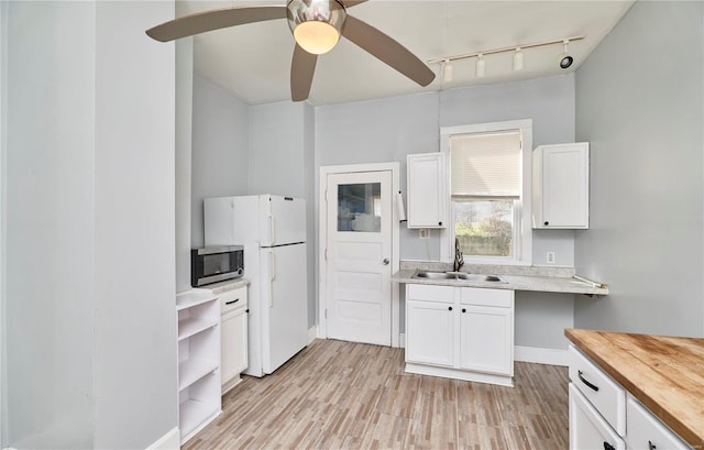 kitchen featuring stainless steel microwave, a sink, butcher block counters, freestanding refrigerator, and white cabinets