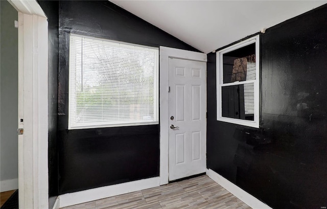 doorway with light wood finished floors, baseboards, and vaulted ceiling