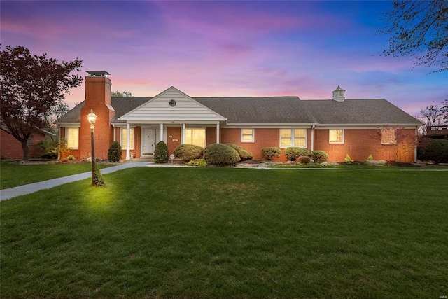 ranch-style home featuring roof with shingles, brick siding, a chimney, and a front lawn