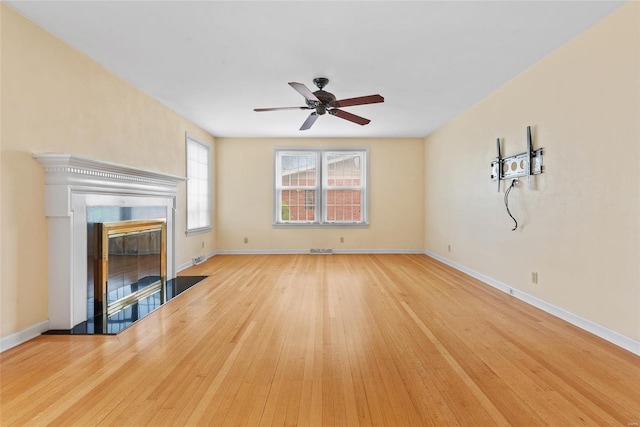 unfurnished living room with baseboards, a ceiling fan, wood finished floors, and a fireplace with flush hearth