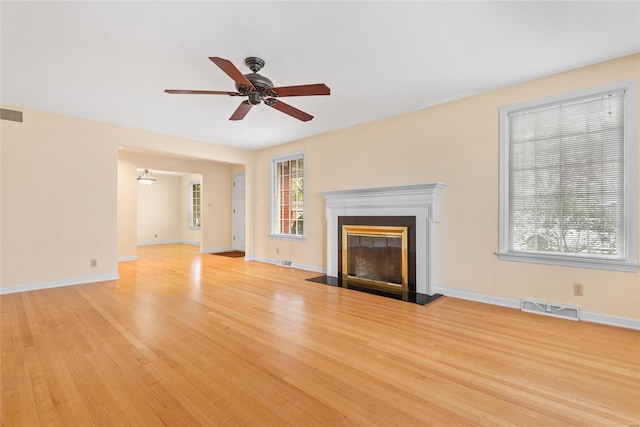 unfurnished living room featuring a glass covered fireplace, baseboards, light wood-style flooring, visible vents, and ceiling fan