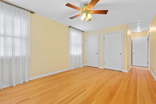 unfurnished bedroom with baseboards, light wood-type flooring, ceiling fan, and two closets