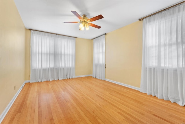 spare room featuring a wealth of natural light, baseboards, light wood-type flooring, and a ceiling fan