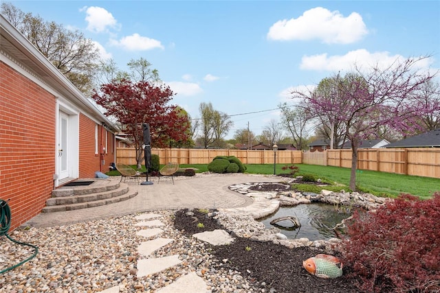 view of yard featuring a patio area, entry steps, a fenced backyard, and a small pond