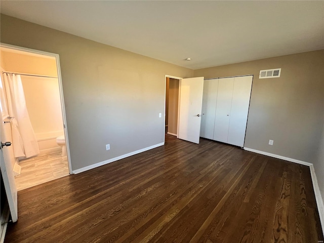 unfurnished bedroom with visible vents, dark wood finished floors, connected bathroom, a closet, and baseboards