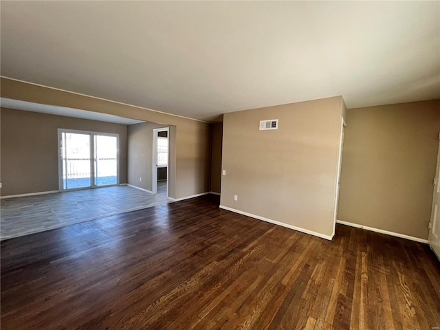 empty room featuring dark wood-type flooring, baseboards, and visible vents
