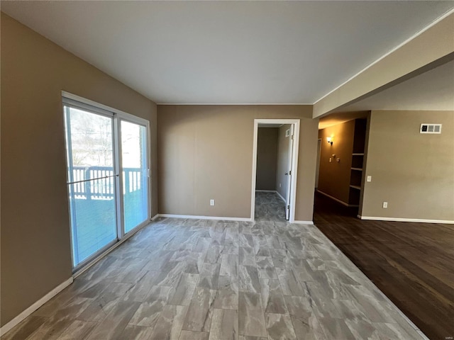 spare room featuring arched walkways, visible vents, baseboards, and wood finished floors