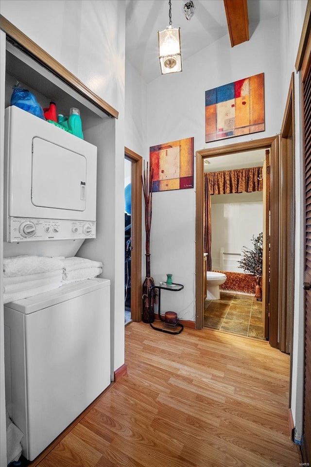clothes washing area featuring baseboards, light wood-style flooring, stacked washer and dryer, and laundry area