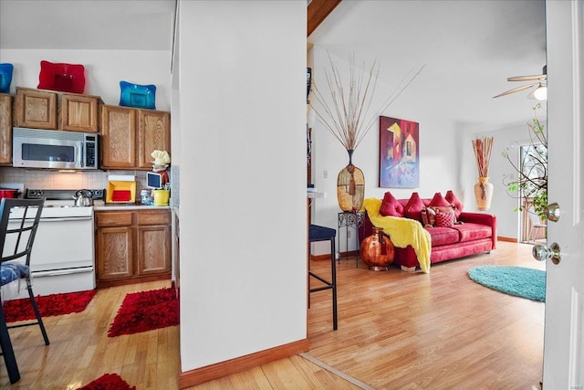 interior space with ceiling fan, light wood-style floors, brown cabinets, stainless steel microwave, and white electric range oven