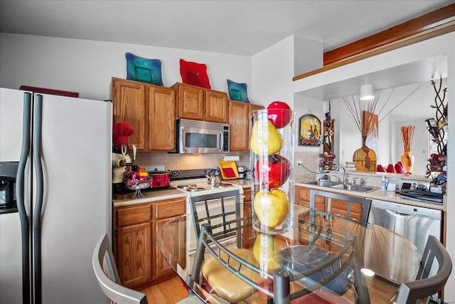 kitchen with light countertops, backsplash, brown cabinetry, stainless steel appliances, and a sink
