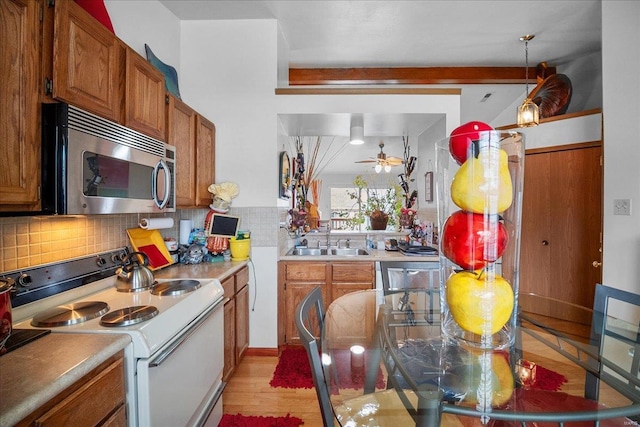 kitchen featuring tasteful backsplash, electric range, stainless steel microwave, a sink, and brown cabinets