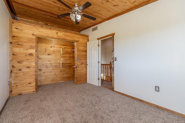 carpeted empty room featuring a ceiling fan, visible vents, wooden ceiling, wood walls, and baseboards