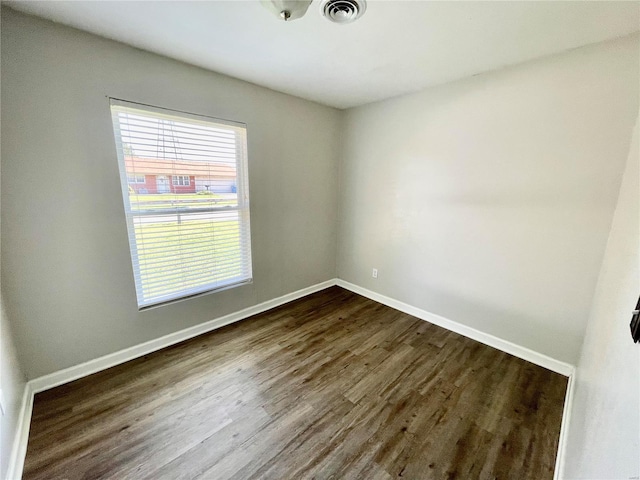 unfurnished room with baseboards, dark wood-style flooring, and visible vents