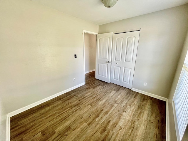 unfurnished bedroom featuring wood finished floors, baseboards, and a closet