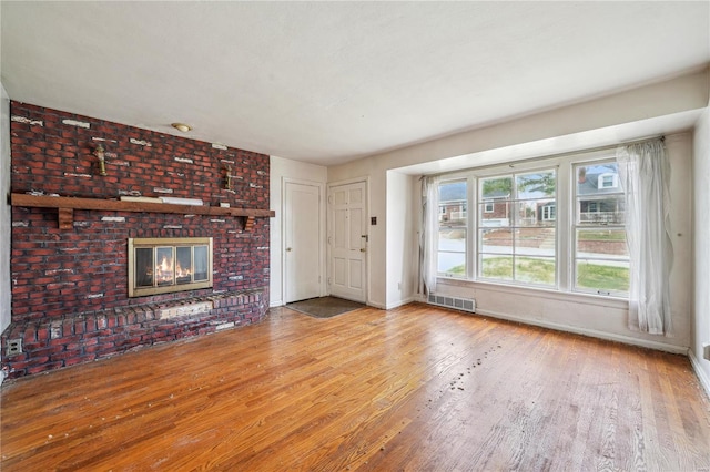 unfurnished living room with wood finished floors, baseboards, visible vents, and a brick fireplace