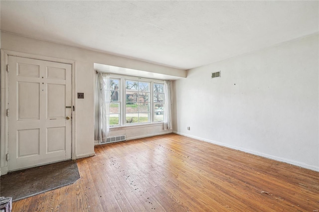 foyer entrance with light wood finished floors, visible vents, and baseboards