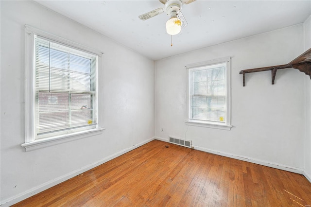 spare room with a wealth of natural light, a ceiling fan, hardwood / wood-style floors, and baseboards
