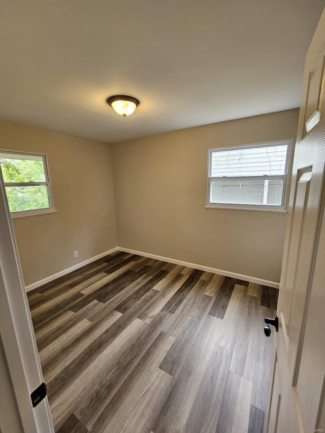 spare room with baseboards and dark wood-style flooring