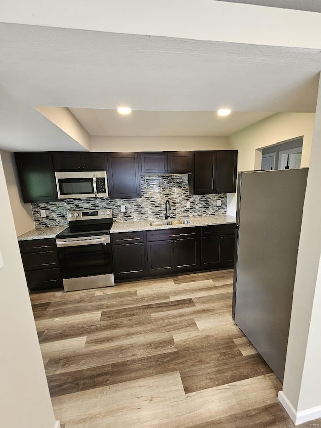 kitchen featuring light wood finished floors, backsplash, appliances with stainless steel finishes, and a sink