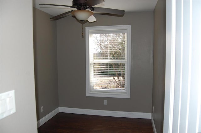 spare room with baseboards, dark wood-style floors, and a ceiling fan