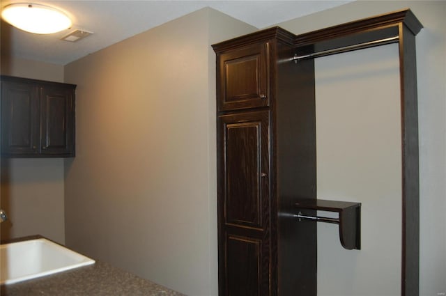 kitchen featuring dark brown cabinetry, dark countertops, visible vents, and a sink